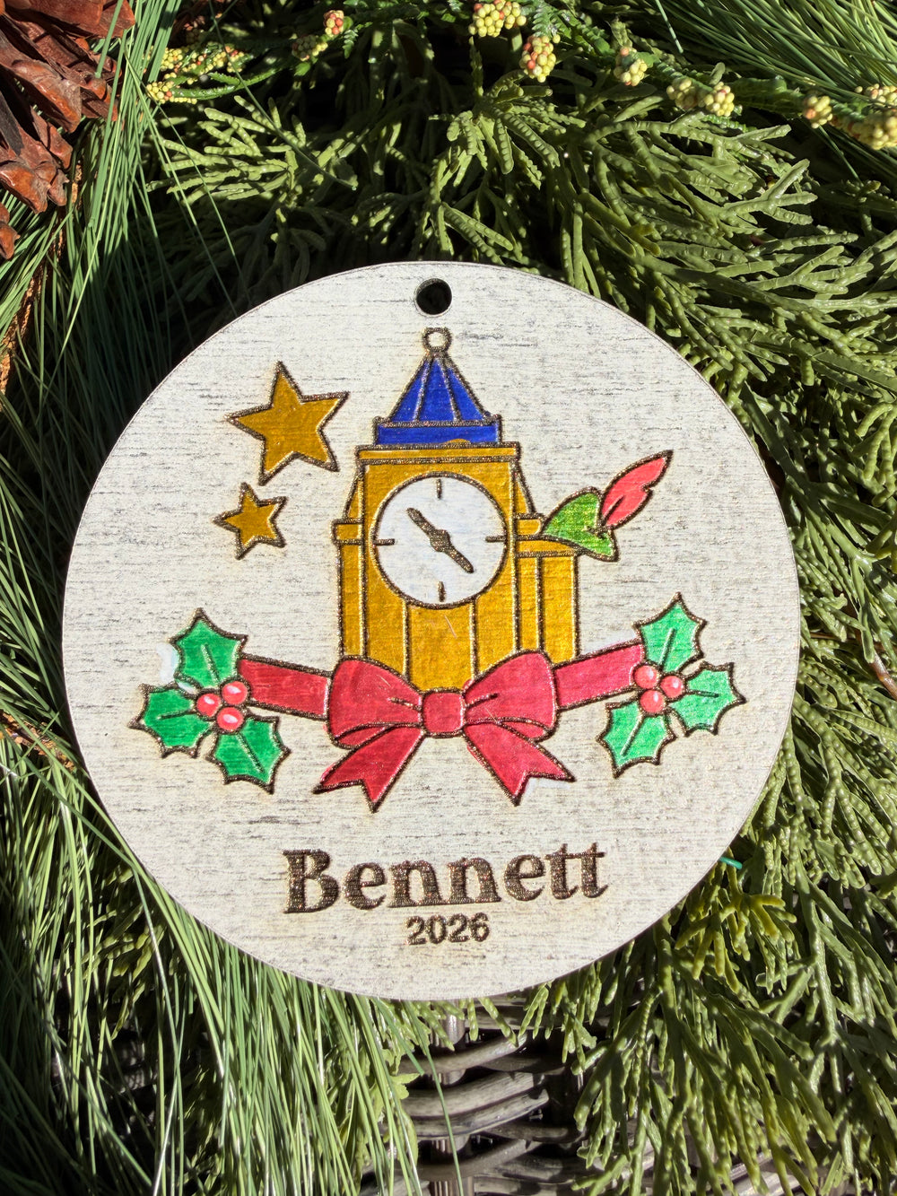 Finished hand-painted Neverland Clock Tower Christmas Ornament on evergreen greenery. Name and year shown are sample personalization.