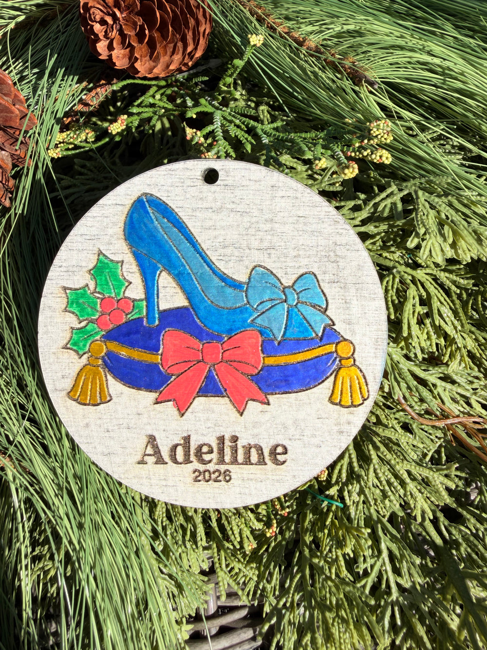 Finished hand-painted Glass Slipper Christmas Ornament on evergreen greenery. Name and year shown are sample personalization.