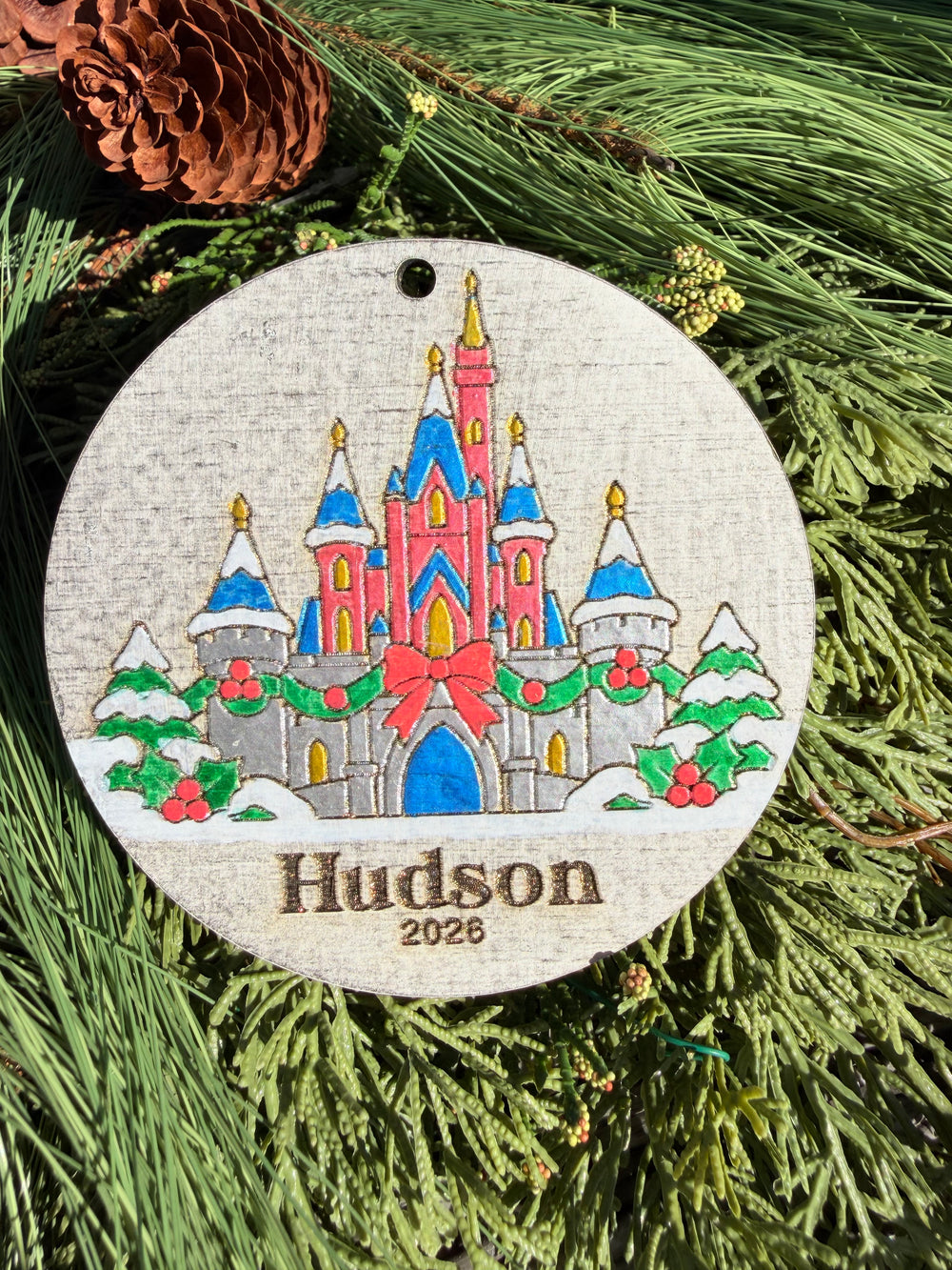 Finished hand-painted Cinderella Castle Christmas Ornament on evergreen greenery. Name and year shown are sample personalization.