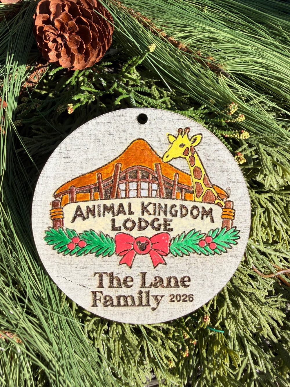 Finished hand-painted Animal Kingdom Lodge Christmas Ornament on evergreen greenery. Name and year shown are sample personalization.