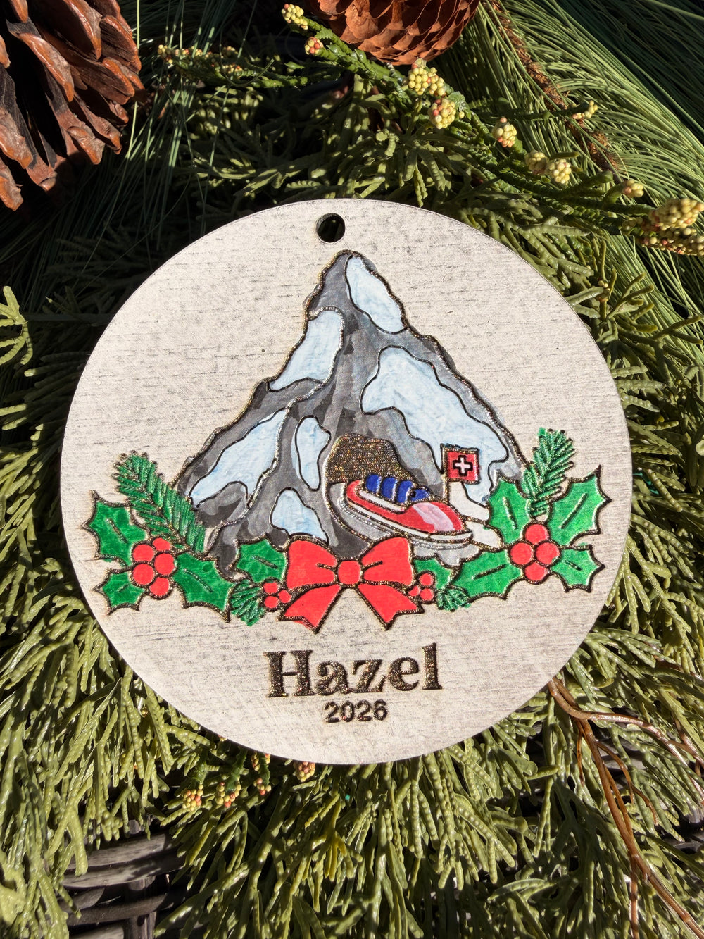 Finished hand-painted Matterhorn Christmas Ornament on evergreen greenery. Name and year shown are sample personalization.