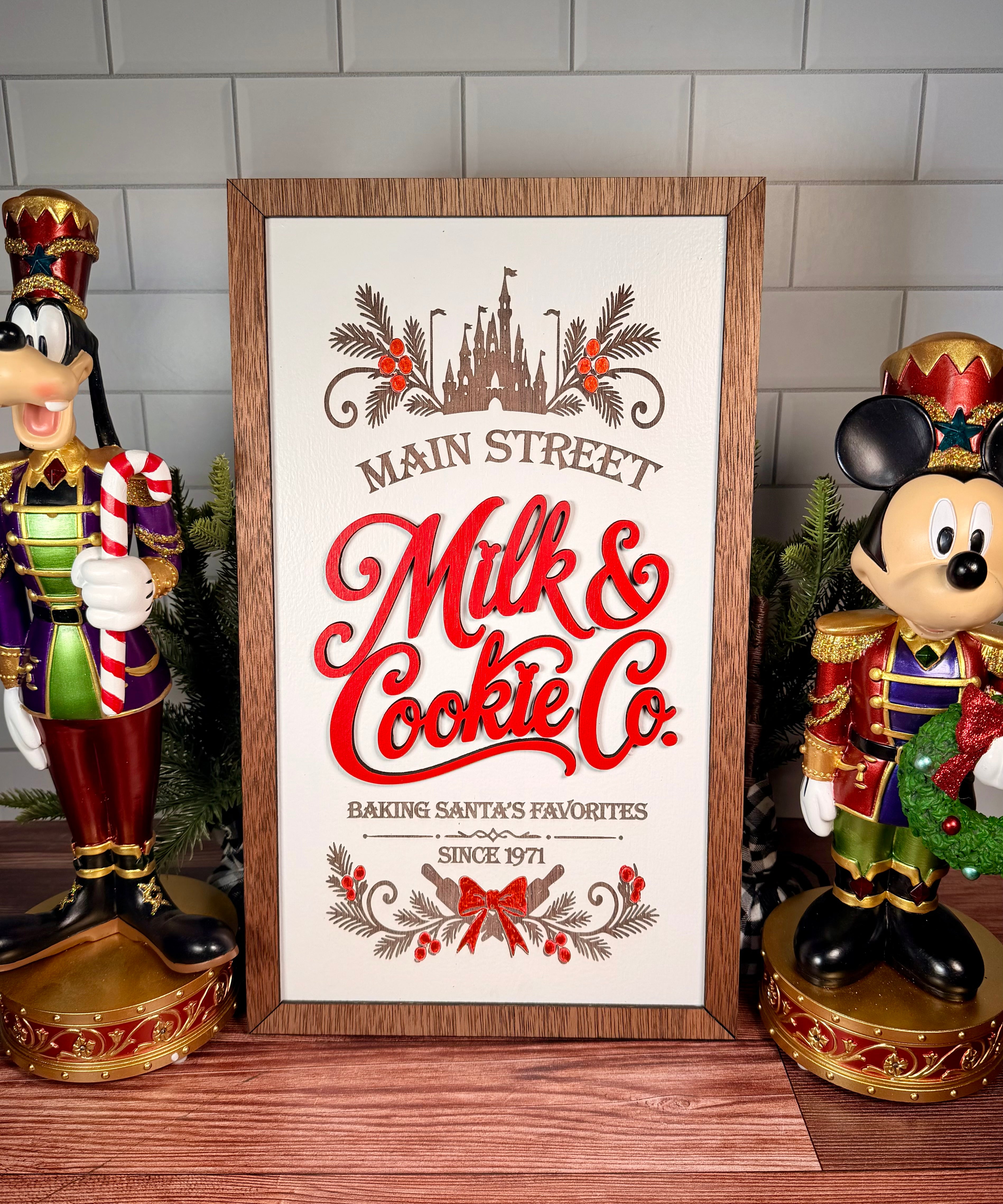 Vertical framed Christmas sign with red Milk & Cookie Co. lettering, castle and evergreen artwork, a cream background and brown wood frame.