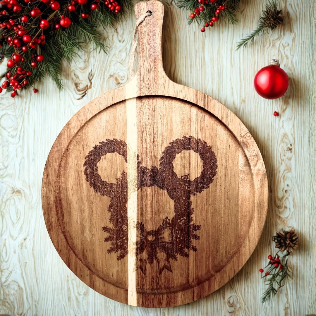 Round acacia charcuterie board engraved with a mouse-shaped pine wreath and bow